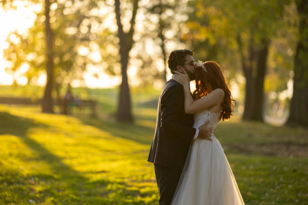 Romantic groom kissing his bride in park on sunny autumn day