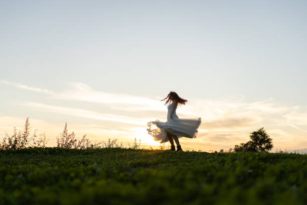 Full length shot of happy bride spinning in nature at sunset