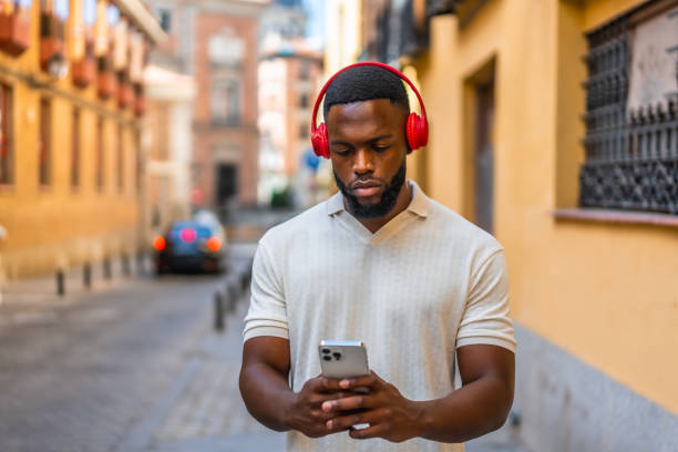 istock African man using mobile phone and headphones walking down street 2181133924