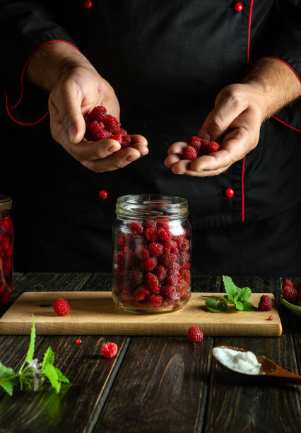 istock Chef hands sorting raspberries before filling a canning jar. Making Rubus idaeus compote on a kitchen counter. Advertising space 2181134195