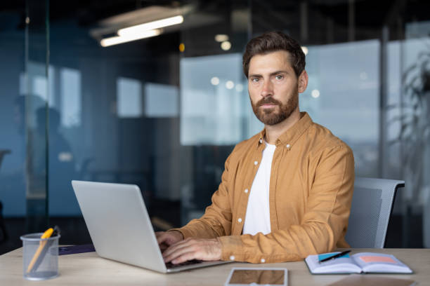 istock Confident mature businessman working on laptop in modern office setup with open notebook and smartphone on desk 2181136968