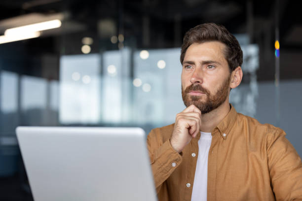 istock Thoughtful professional man contemplating ideas with laptop in modern office 2181137010