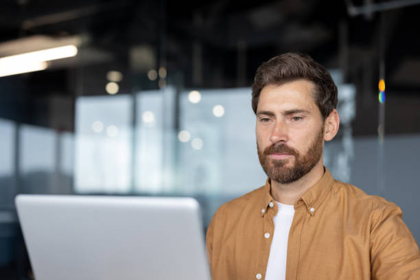 istock Focused man with beard working on laptop in modern office environment, showcasing productivity and concentration in contemporary workspace 2181137051