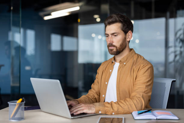 istock Serious man at work with laptop inside office, thinking businessman typing on keyboard, preparing electronic report, mature worker programmer, coding new software at workplace 2181137945