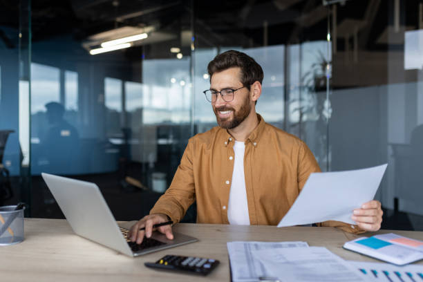 istock Satisfied and confident financier accountant with paper work inside the office, smiling man works with documents and bills, successful businessman compares statistical data uses laptop and calculator 2181138075