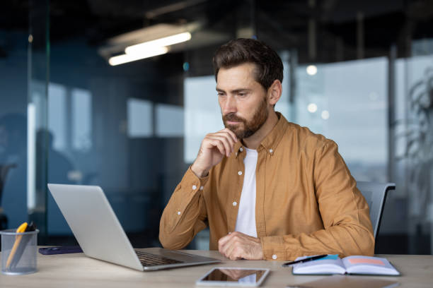 istock Focused mature businessman working on laptop in modern office setting with notebook and phone on desk indicating a professional work environment and thoughtful analysis 2181138563