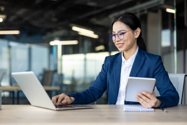 istock Confident Asian businesswoman using laptop and tablet in modern office setting 2181146198