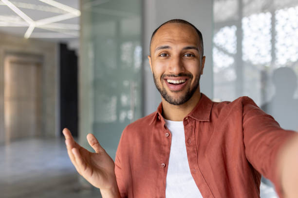 istock Smiling man taking a selfie during a video call with his smartphone in a modern office environment 2181152199
