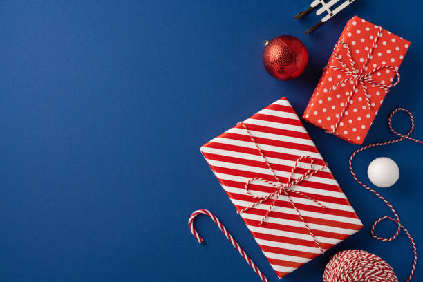Colorful wrapped presents with festive designs are set on a top view blue backdrop, featuring a candy cane and Christmas ornaments