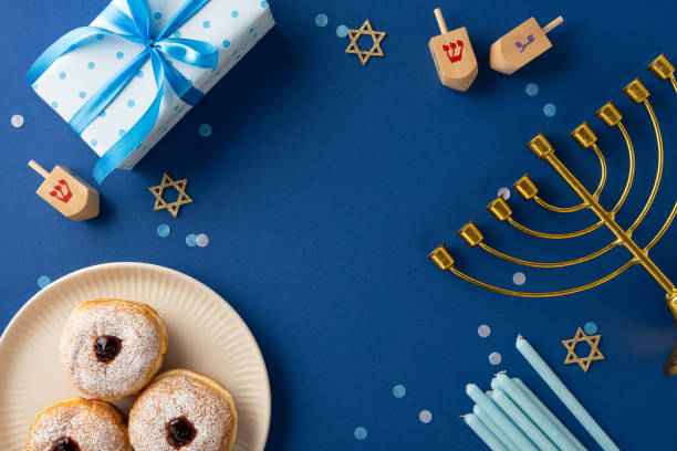 istock A top view of a Hanukkah celebration setup featuring a menorah, dreidels, doughnuts, and a gift. The blue theme and decorations emphasize the festive spirit of the Hanukkah season 2181152766