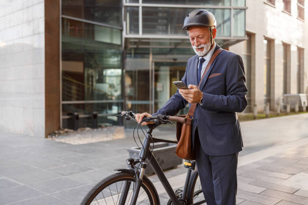 istock Old male entrepreneur checking messages over mobile phone while standing with bicycle on city street 2181154486