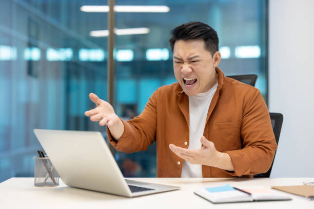 istock Frustrated asian businessman expressing anger while working on laptop in modern office environment 2181157507