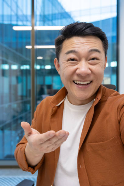 istock Asian businessman smiling during video call using phone in modern office building, wearing casual attire, showcasing confidence and positive spirit amidst professional setting. 2181162404