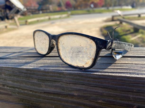 Close-up of broken red eyeglasses lying on the asphalt near a concrete wall. One lens has fallen out of the frame. The image symbolizes loss, failure, fragility, and forgotten moments in everyday urban life. Ideal for illustrating concepts of vision, mistakes, accidents, or emotional vulnerability.
