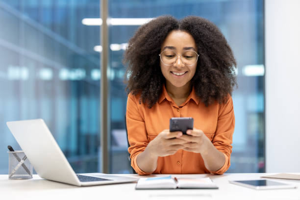 istock Young woman working in office environment using smartphone while smiling. Engaged in digital communication, multitasking with laptop and tablet. Capturing positive and productive atmosphere. 2181165567