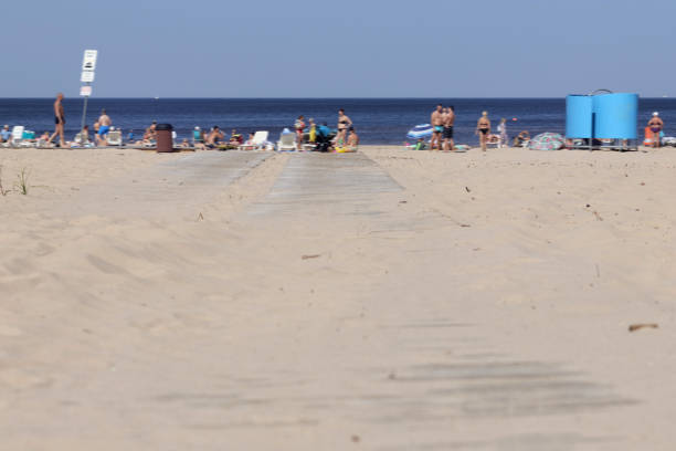 Old white woman in a swimsuit and a bandana sits in a tourist chair on the beach near the sea, unrecognizable people are resting behind