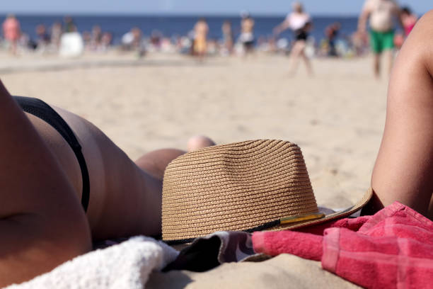 woman sunbathing on the beach with a sun hat next to her