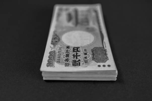 A stack of 2000 yen bills in grayscale lies on a black surface, symbolizing economic recession and financial struggles, highlighting the theme of monetary devaluation and crisis