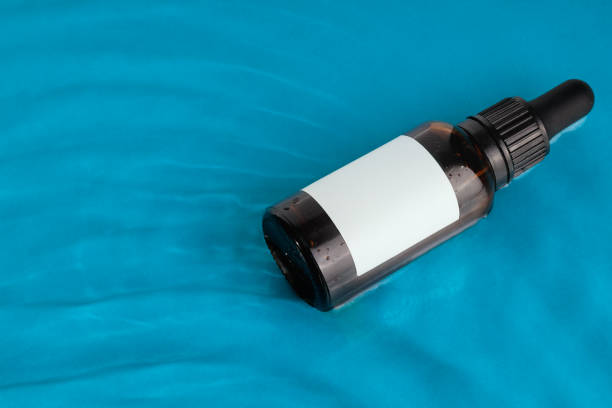 istock Amber glass dropper bottle with a blank label floating on a blue water surface ideal for branding mockups 2181209823
