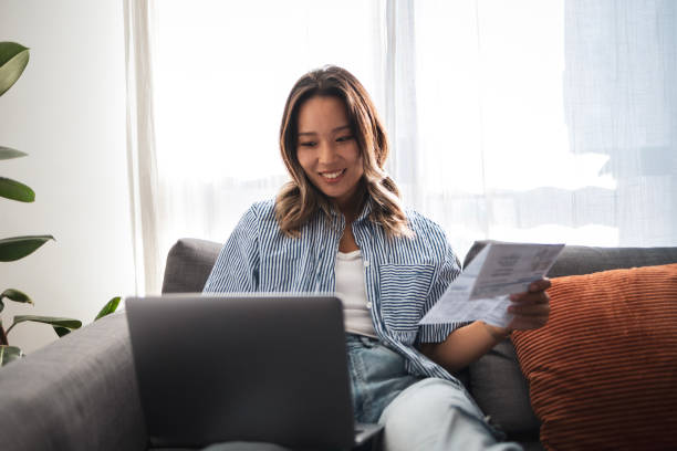 istock Smiling woman working on a laptop at home with documents in hand 2181212235