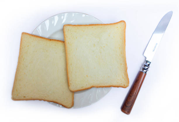 Clean, minimalist image of two slices of bread on a white plate, accompanied by a knife. Ideal for illustrating simple meals, culinary articles, or breakfast themed visuals