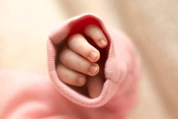 istock Tiny hand peeking from pink fabric, showcasing delicate fingers in soft light 2181231489