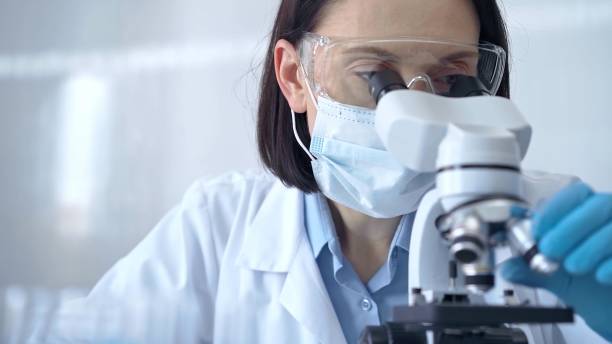 istock Female scientist in lab goggles, protective mask and gloves is using microscope in laboratory. Science concept 2181238027