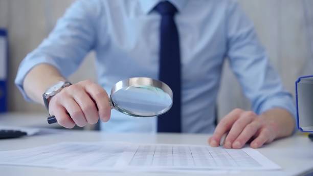istock Businessman is carefully examining financial documents with a magnifying glass, highlighting the importance of thorough analysis in business. Audit and taxes 2181242922