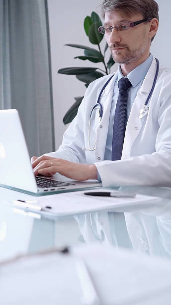 istock Male physician in white coat focused on laptop data in a modern clinic office while analyzing patient information on laptop. Medicine concept 2181263744