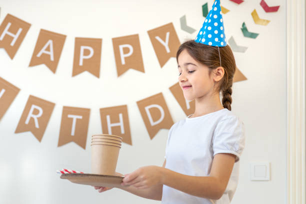 Birthday concept. Preparation for the birthday. Festive paper cups. High quality photo. Paper plates, cups and straws. Girl preparing for birthday. Happy birthday in the background.