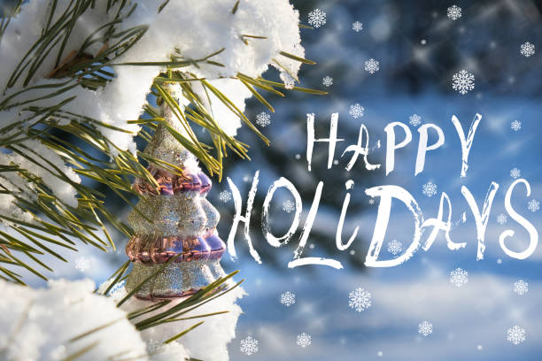 Happy Holidays text. Christmas tree with decorations. Snowing. Snow covered trees in a winter landscape. Merry Christmas and Happy New Year