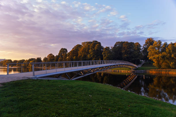 istock A modern pedestrian bridge stretching over a calm river, surrounded by lush greenery and trees. The bridge has a sleek, minimalist design. Sunrise or sunset. 2181287093