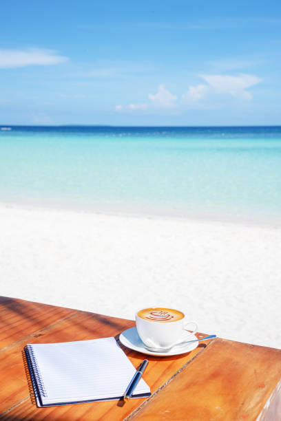 Cup of coffee and notebook on the table at tropical paradise beach cafe bar