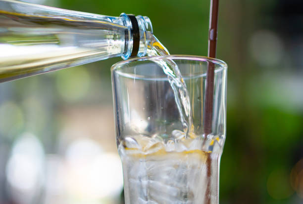 istock Freshly poured clear,sparkling liquid beverage flowing into a transparent glass against a blurred green natural background. Concept of enjoying a cold,crisp drink outdoors in nature. 2181297979