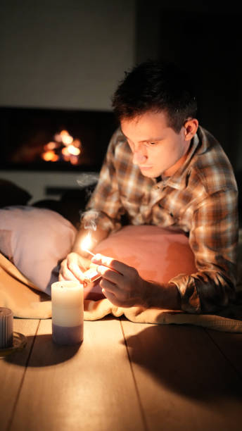 istock A man lights a candle in a cozy setting, with a warm fire glowing in the background. 2181301830