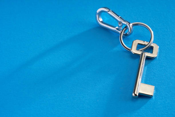 Silver house key with house keychain on blue background with copy space.