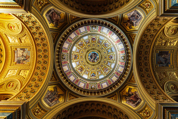 Budapest, Hungary - December 6, 2018: It is an exquisite example of artistic brilliance, adorned with intricate frescoes and gilded details. The dome's vibrant colors and celestial themes create a captivating atmosphere, reflecting the basilica's spiritual significance. This architectural highlight draws visitors' gazes upward, enhancing the overall grandeur of the interior space.