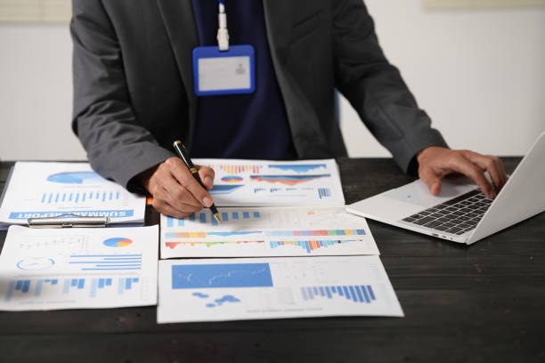 istock A focused businessman sits at his office desk, analyzing a paper chart while working on his laptop. He examines financial and marketing reports, concentrating on data for strategic decision-making. 2181309548