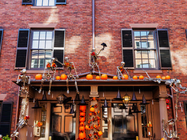 Boston, Massachusetts, USA - October 22, 2024: A Beacon Hill townhouse decorated for the Halloween holiday. Human skeletons, witch's black hats and pumpkins cover the whole front entrance of the building. Beacon Hill is a historic neighborhood in Boston, Massachusetts, and the hill upon which the Massachusetts State House resides. Federal-style rowhouses, narrow gaslit streets and brick sidewalks adorn the neighborhood, which is regarded as one of the more desirable and expensive in Boston.
