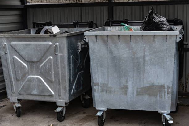 istock Two metal garbage containers stand side by side, one filled with a black garbage bag and miscellaneous waste while the other is empty, located in a waste collection site during dusk 2181315376