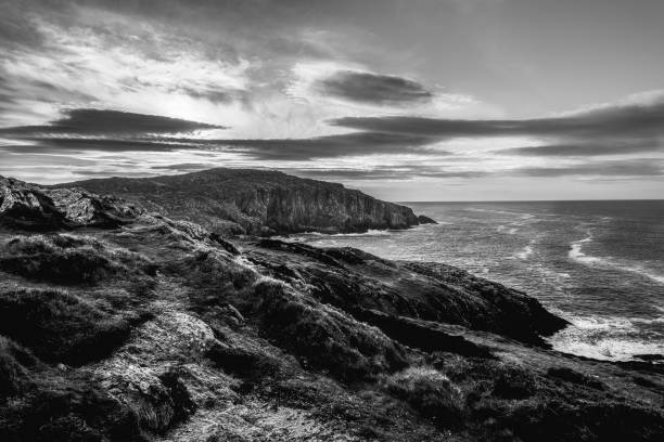 istock The setting features a striking black and white coastal landscape, highlighting rugged cliffs and the turbulent ocean under a dramatic sky at dusk. 2181316125