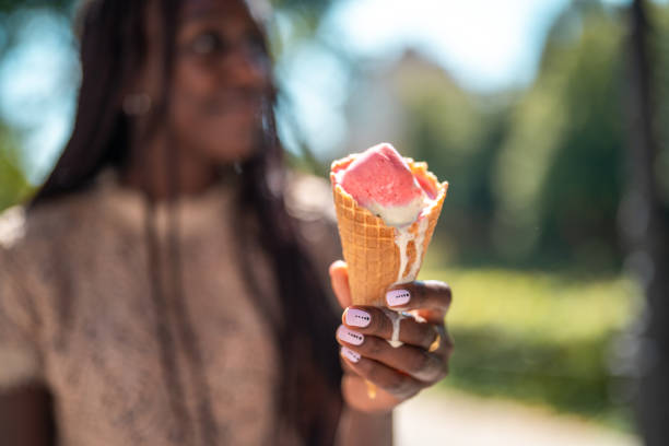 A black woman enjoys a sunny day outdoors holding a waffle cone with melting ice cream, symbolizing summer treats and leisure moments.