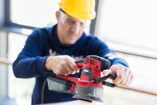Carpenter sanding wooden railing with a electric orbital sander
