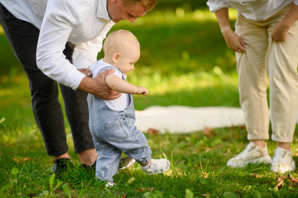istock Child walks in park on grass, learning to walk and taking his first steps, close-up. Infant holding his dad hands goes to meet his mom. Concept of happy family, family vacation, first steps. 2181339702