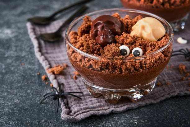 istock Halloween party chocolate puddings or Panna Cotta with brownie crumbles and chocolate sculls served in clear glass on grey dark background. Party idea for Halloween. 2181340708