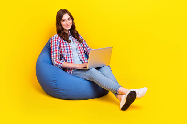 istock Full body photo of young pretty programmer developer woman sitting beanbag use computer working freelancer online isolated on yellow color background 2181340974