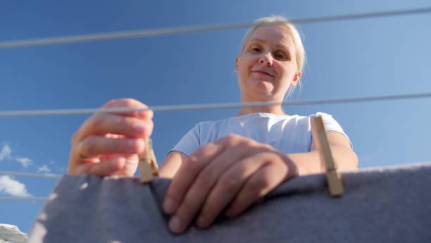 A woman secures clothes on a line with clothespins, viewed from a low angle against a clear blue sky. High quality photo