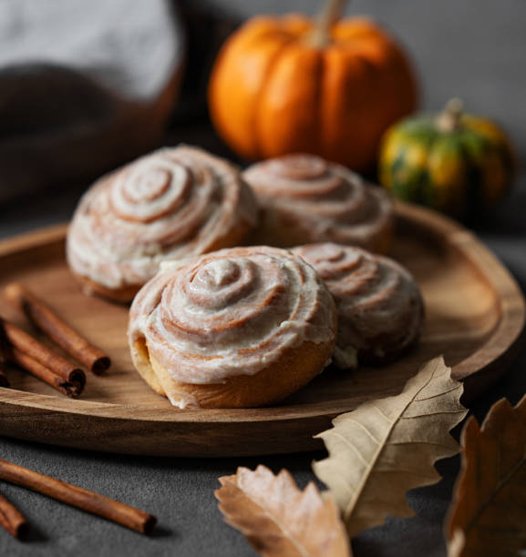 Sweet rolls with cinnamon and icing on a wooden board on a dark background with pumpkin.