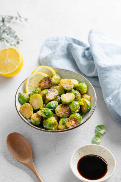 istock Fried brussels sprouts in a bowl with soy sauce, lemon and sesame on a light background with spoon, herb and napkin. 2181358798