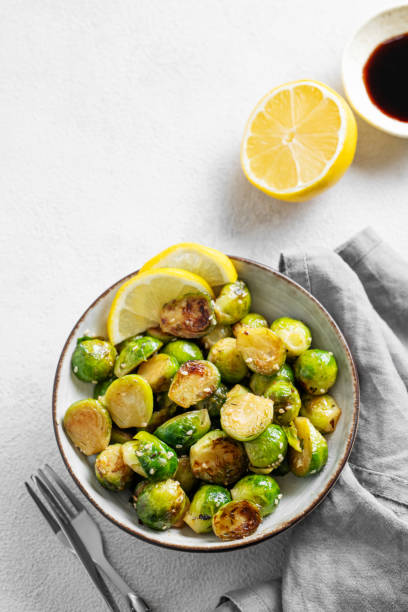 istock Fried brussels sprouts in a bowl with soy or balsamic sauce, lemon and sesame on a light background with fork and napkin. 2181358911